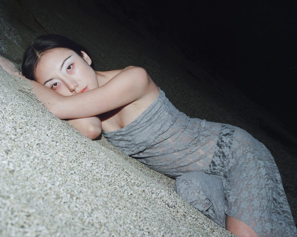 woman lying down on a beach wearing a grey laced dress