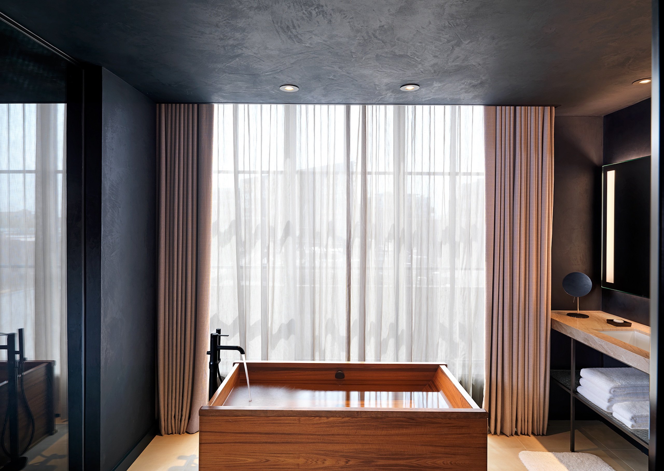 bathroom with wooden tub in front of a large window with a sheer curtain
