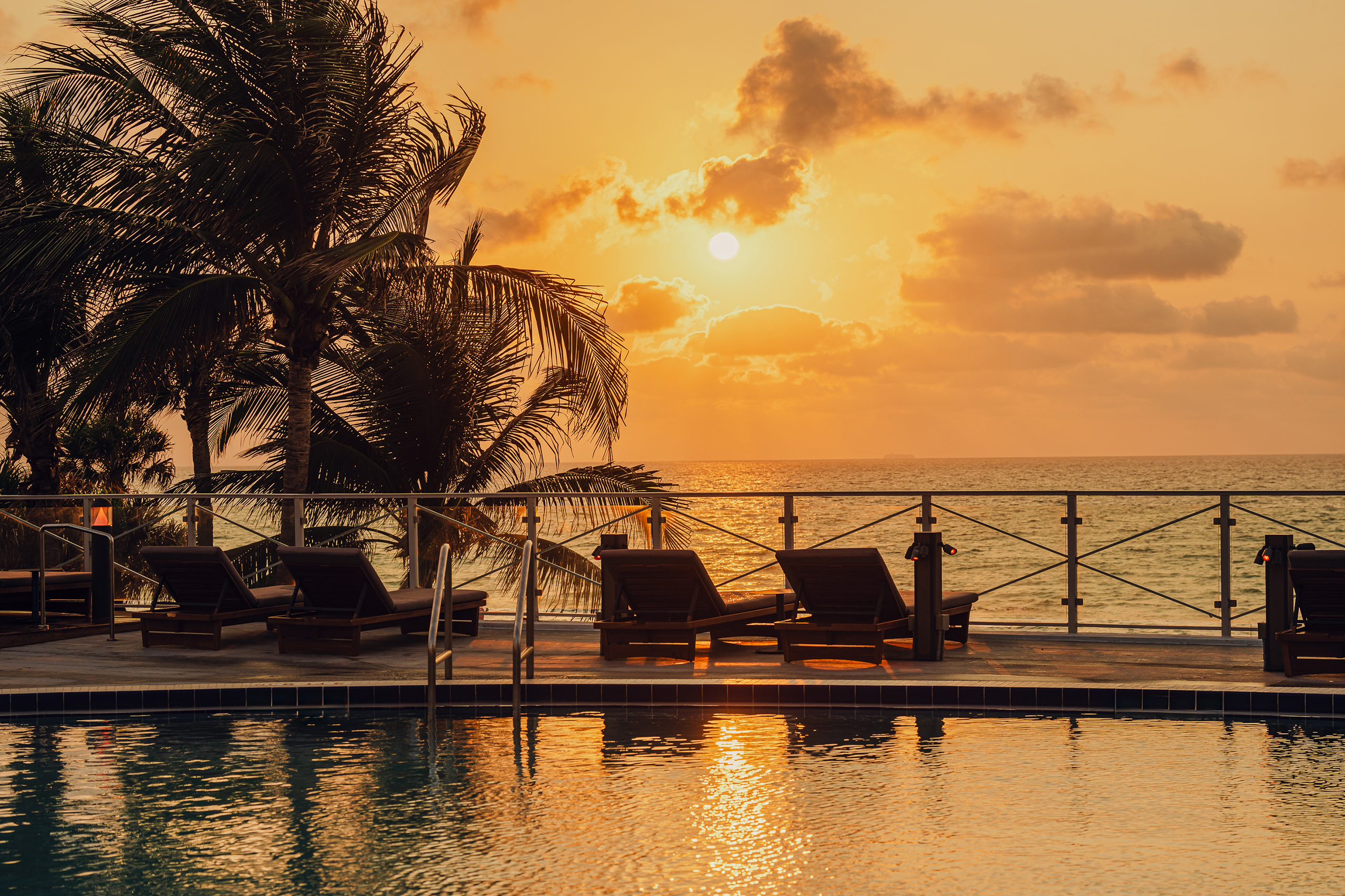 Round swimming pool and beach chairs with the beach view at sunset