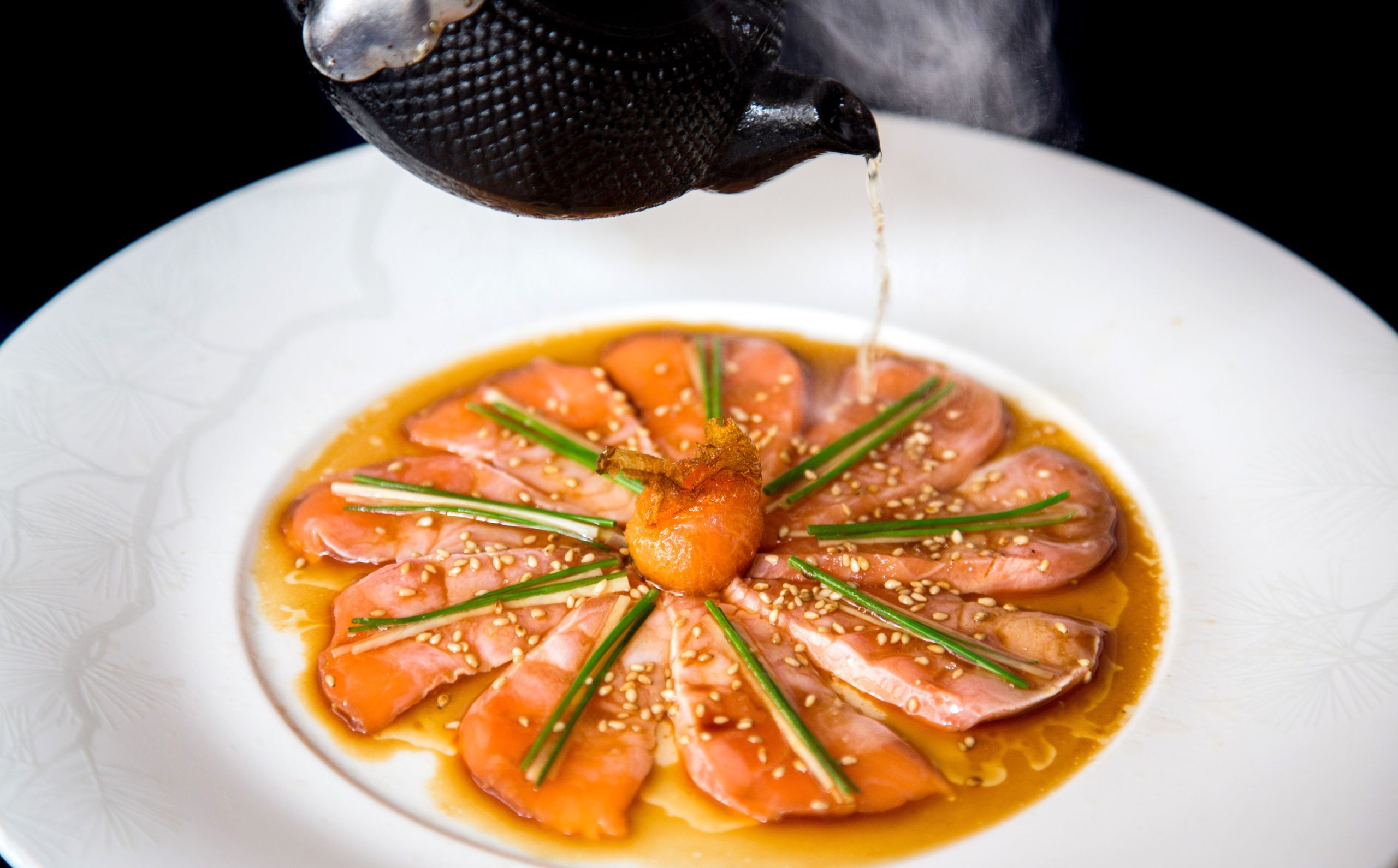 Cured salmon spread out on a plate with sesame seeds, chives, and tea
