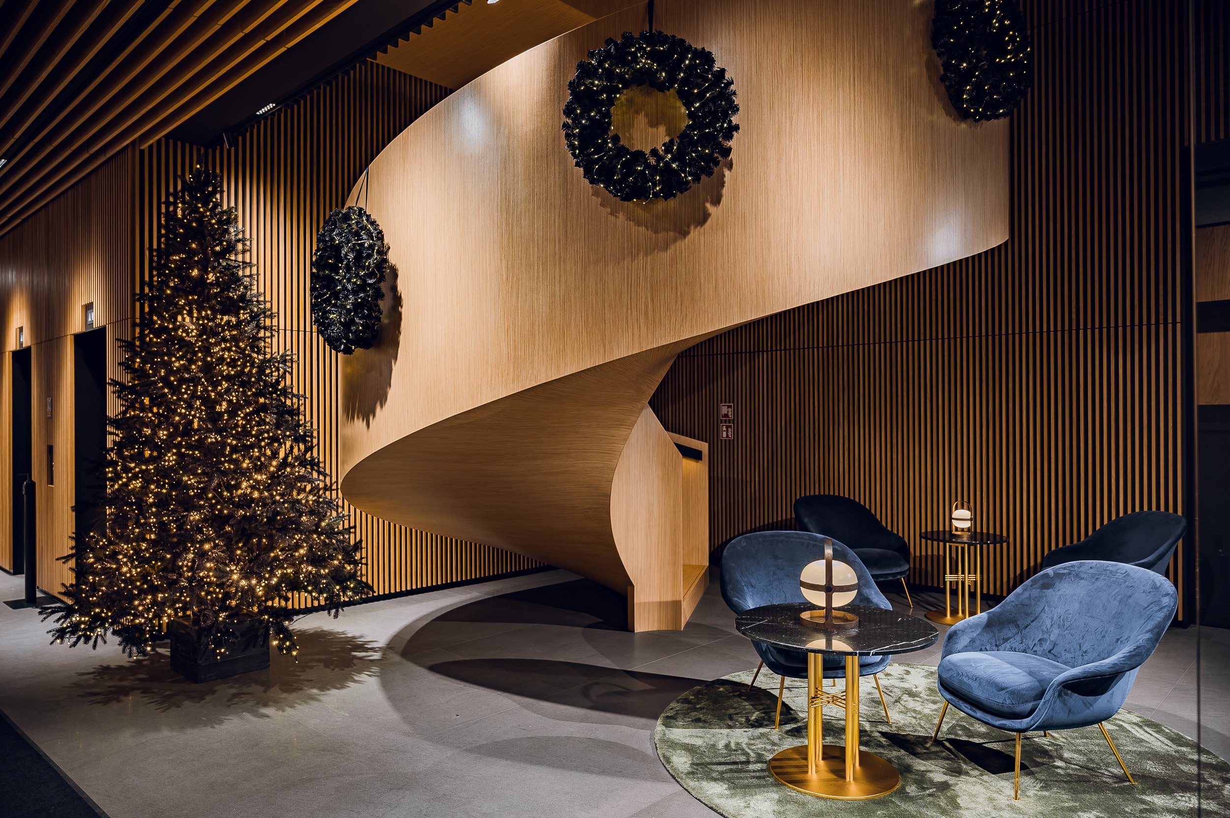 A charming Christmas trees next to a winding spiral staircase in a modern style lobby for holiday season